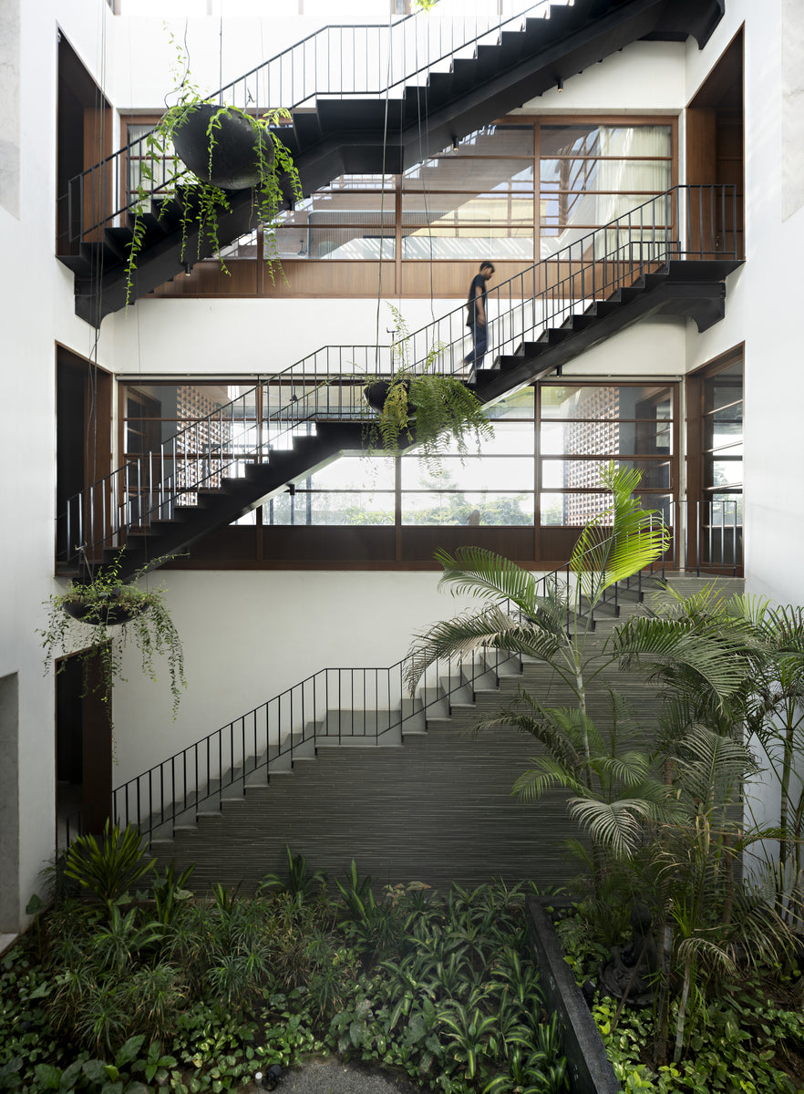 Three-storey courtyard void crossed by steel stairs, hanging planters and a figure descending