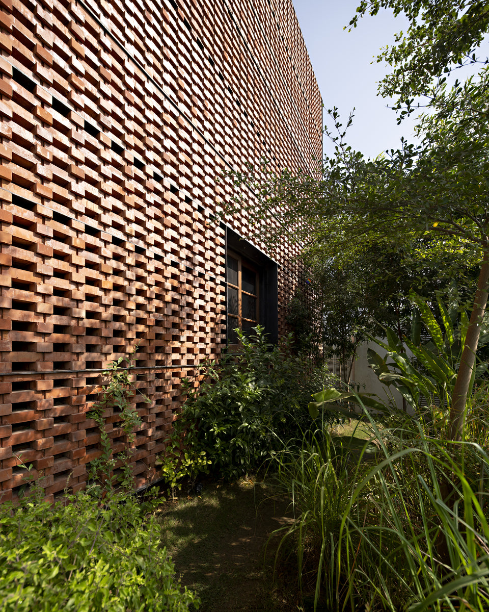 Corbelled brick jaali in raking sunlight along a densely planted side garden