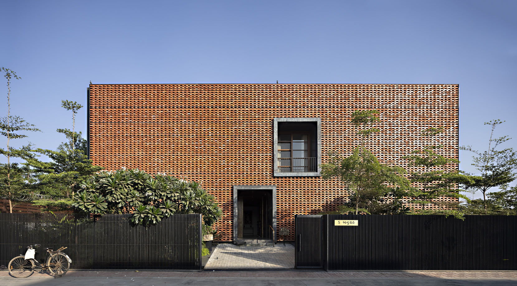 Street elevation behind a dark metal gate, brick jaali unbroken but for one framed window