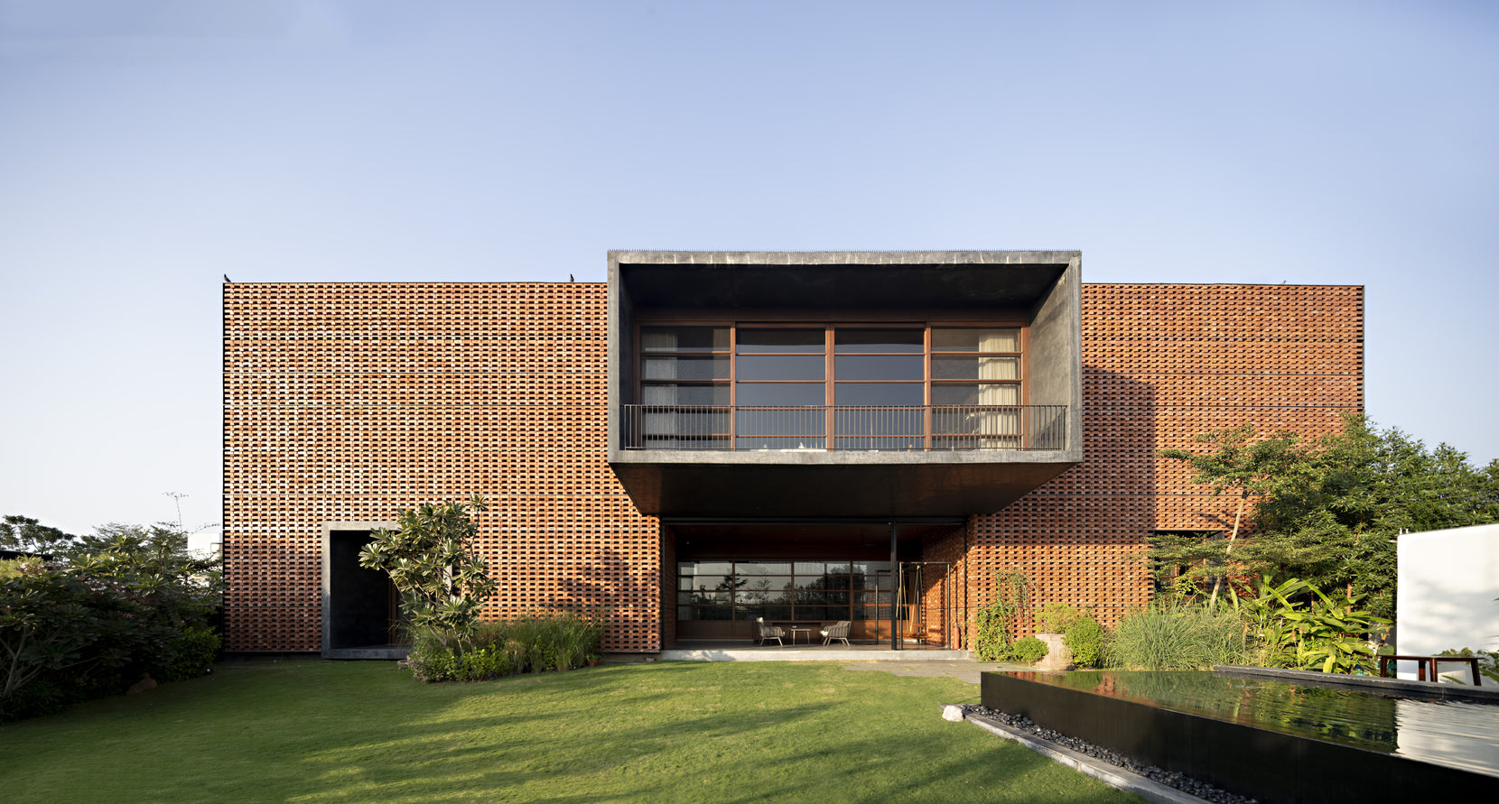 Garden front with the concrete balcony recessed into the brick, beside a dark water body