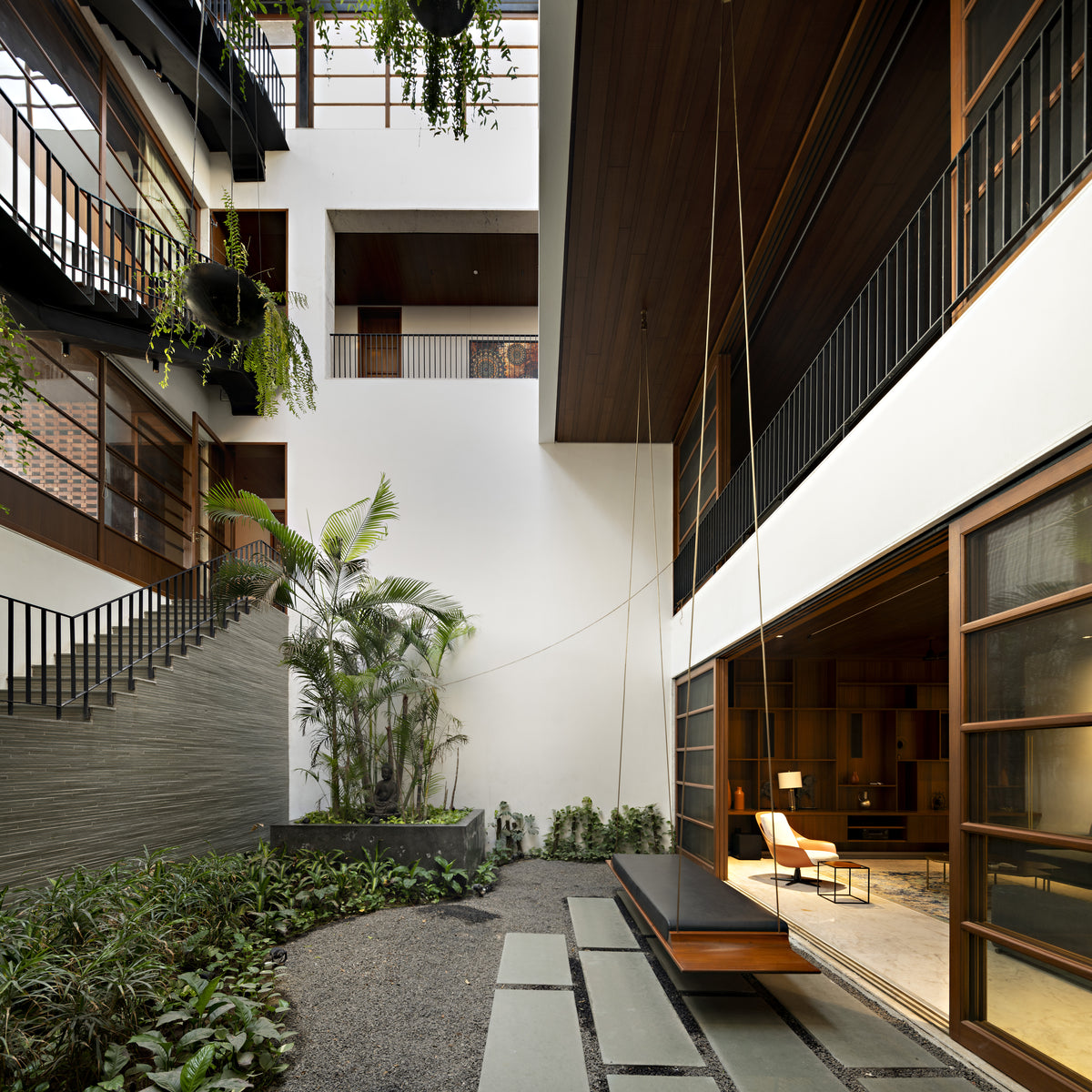 Courtyard at ground level with a hanging swing seat, palms and gravel beside the glazed living room