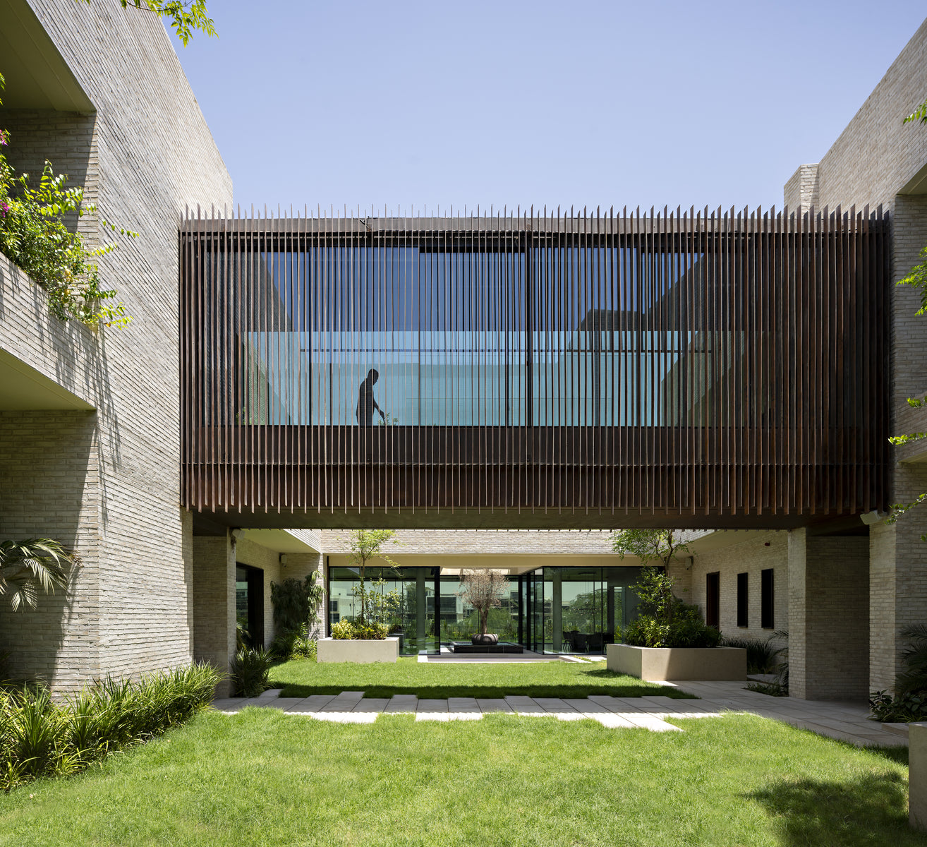 Timber-louvred bridge spanning the courtyard lawn between sand brick wings