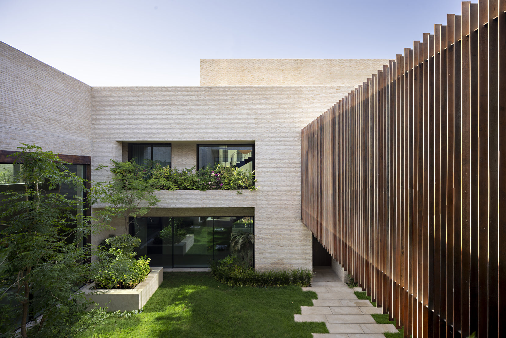 Sand brick wings meeting a screen of vertical bronze fins beside the courtyard lawn