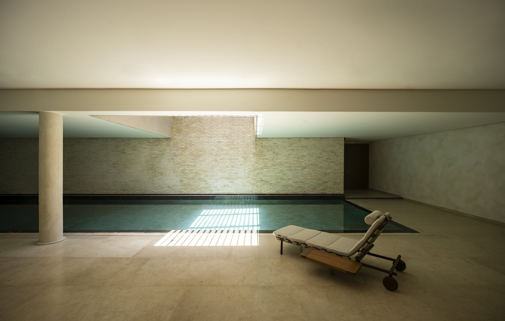 Basement pool lit by a slot of daylight, a single lounger on the stone deck