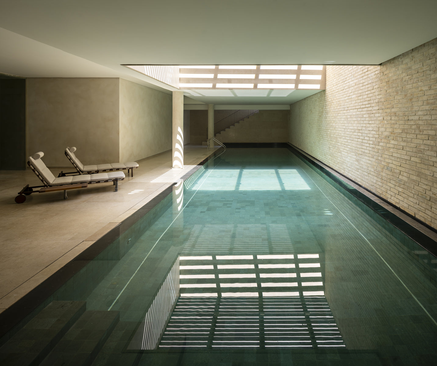 Indoor lap pool below a louvred skylight, its bars reflected across the green water
