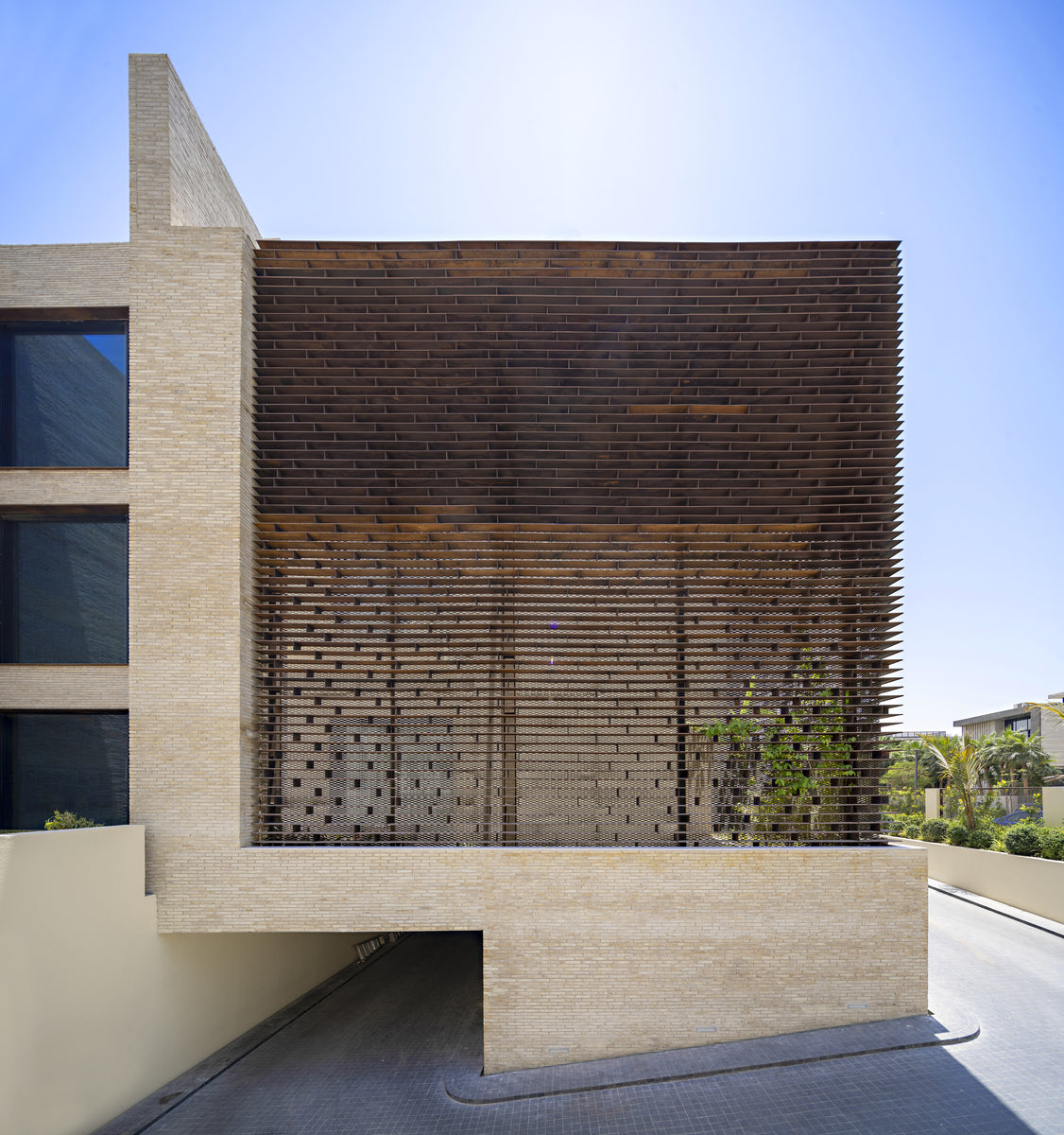 Corten lattice screen set into the sand brick facade above the ramped basement entry