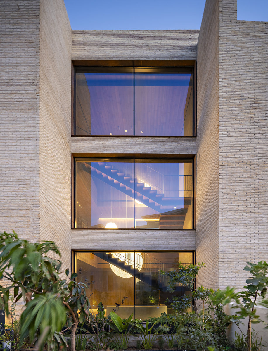 Stacked windows in sand brick revealing the internal stair, seen from the planted garden