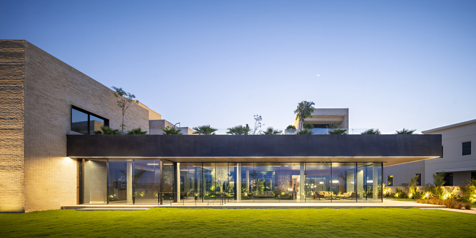 Ishtika's garden elevation at dusk, a long glazed room under a dark planted roof band