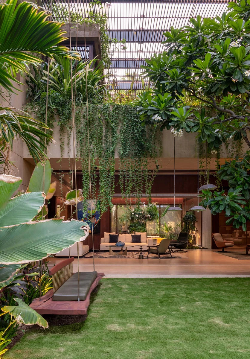 Kasaya house courtyard in Ahmedabad, with a timber swing, hanging creepers and lawn under a louvred canopy