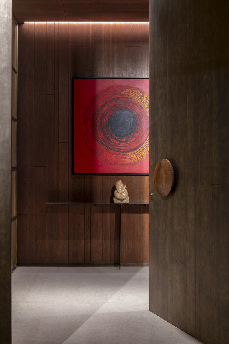 Entrance foyer with a red circular canvas above a slim console, seen past a pivoting bronze-clad door