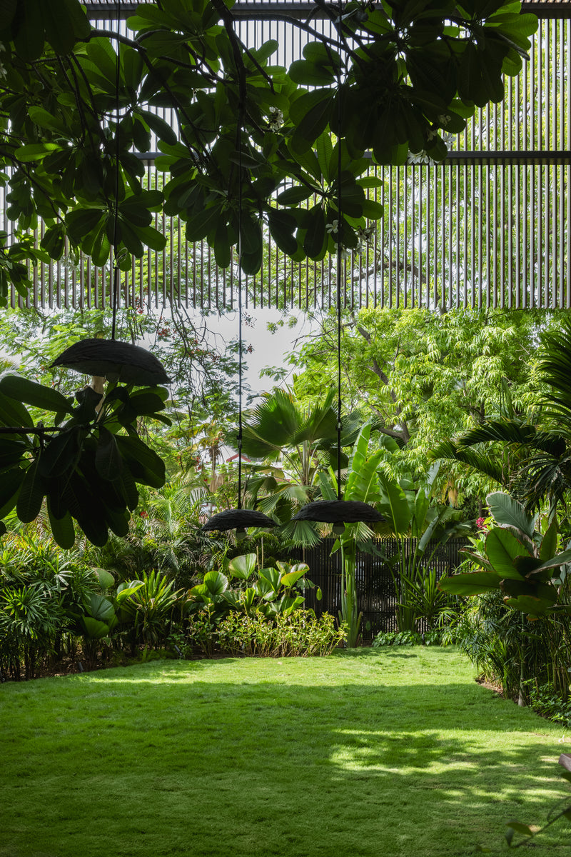 Black woven parasols suspended over the garden, with palms and a louvred screen behind