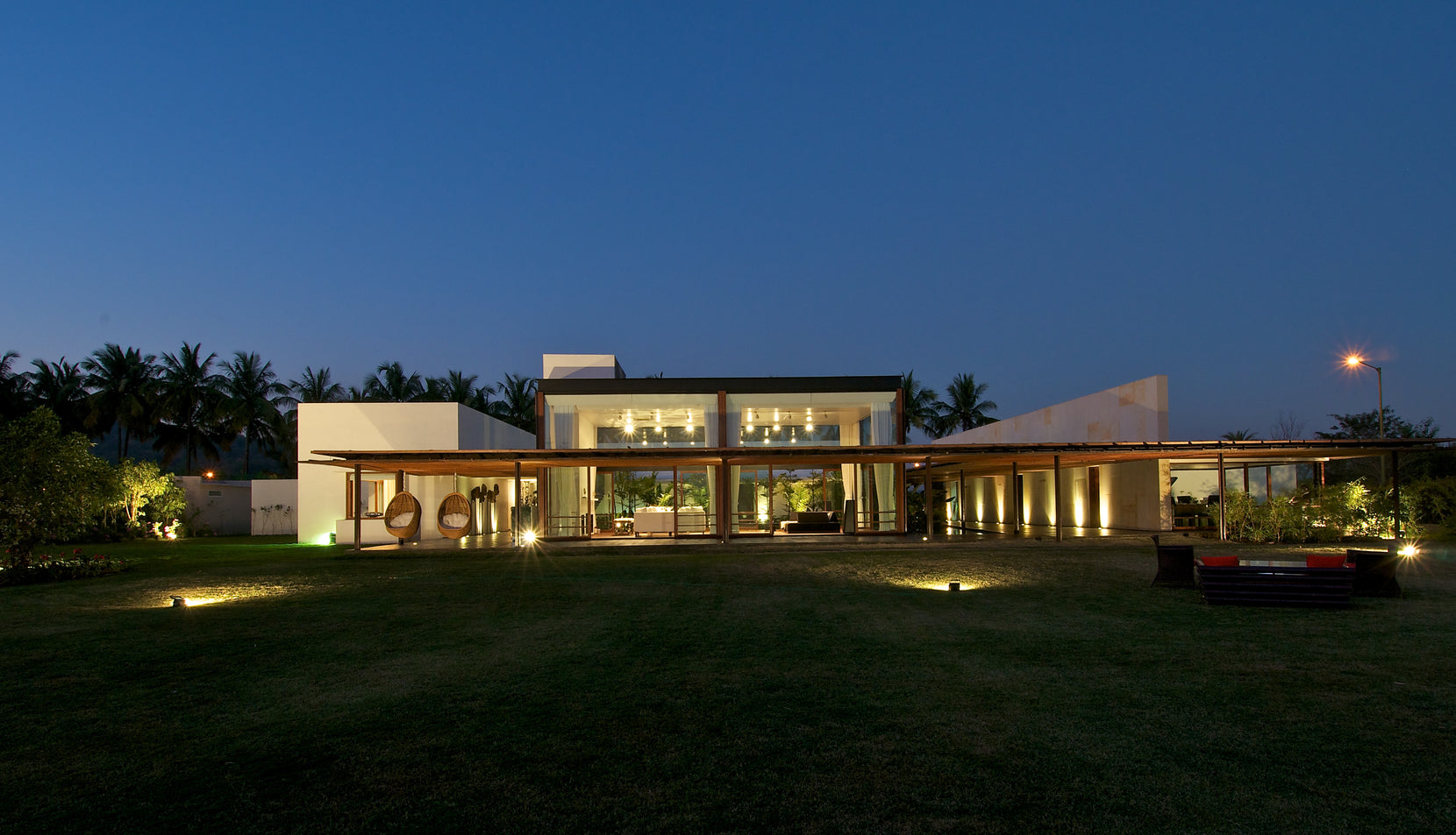 Khadakvasla House at dusk, lit rooms spreading along the lawn beneath a flat roof