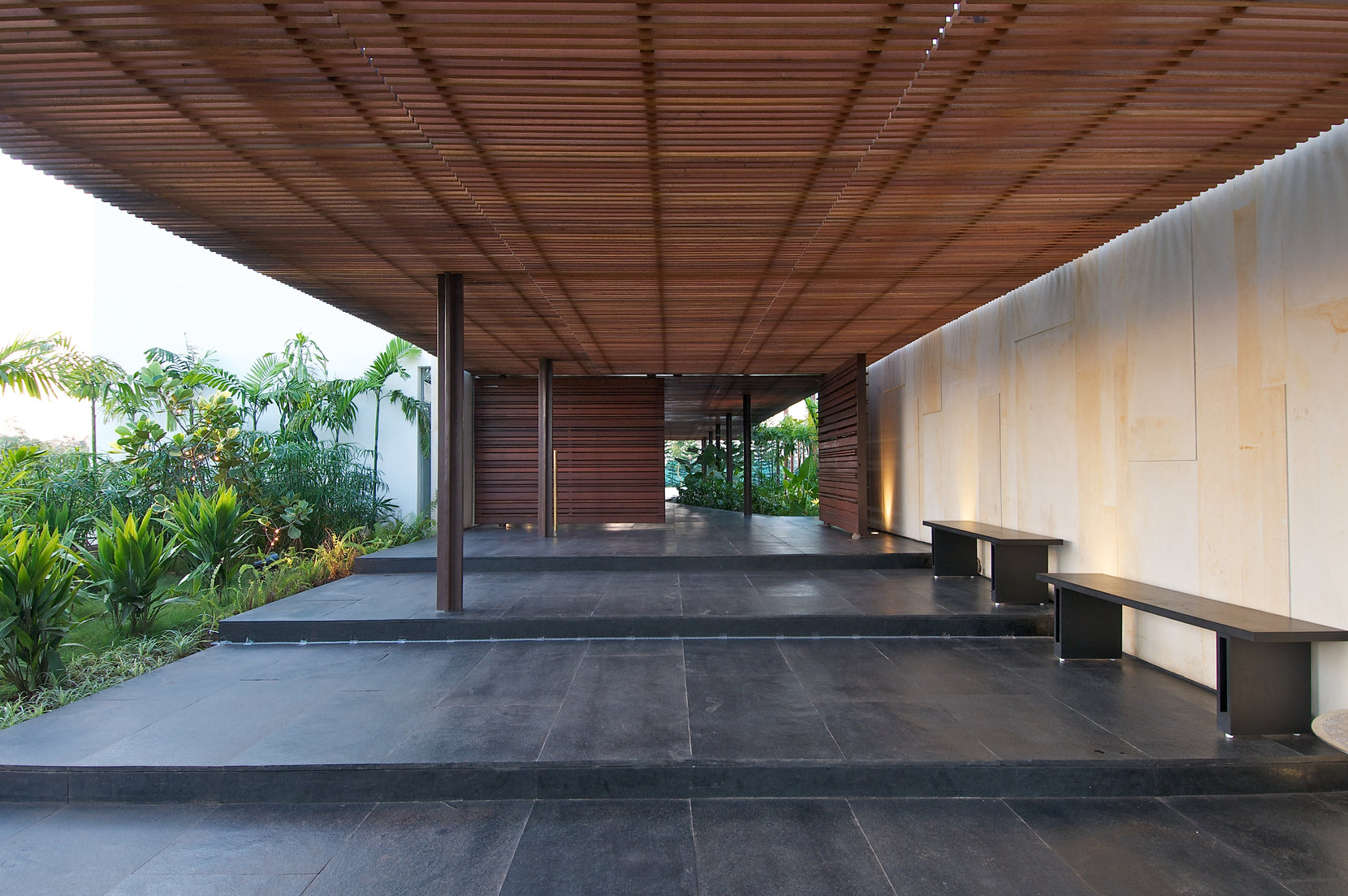 Covered walk with a timber-battened ceiling, benches set against a sandstone wall