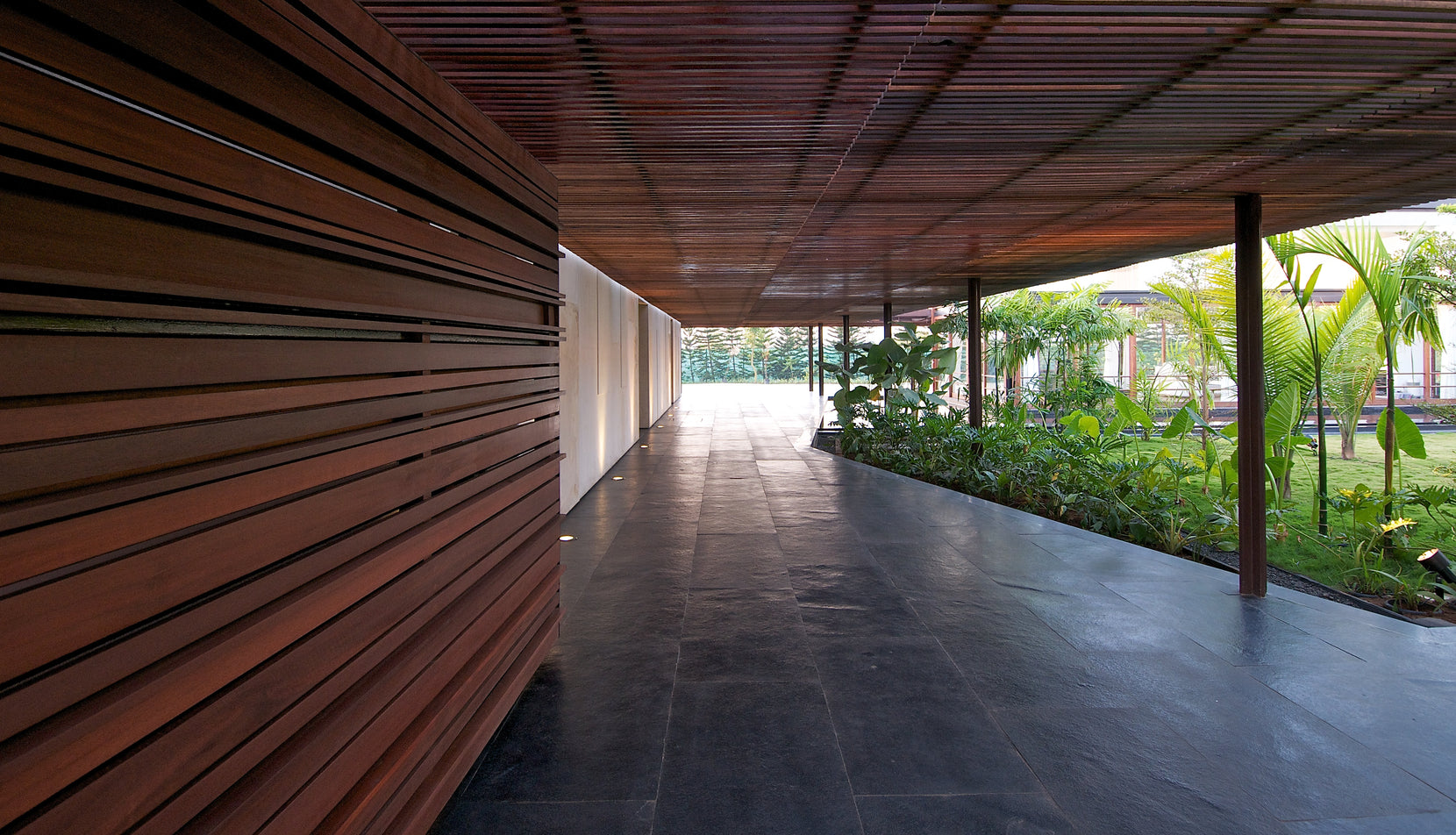 Corridor beside a horizontally slatted timber wall, palms in the courtyard alongside