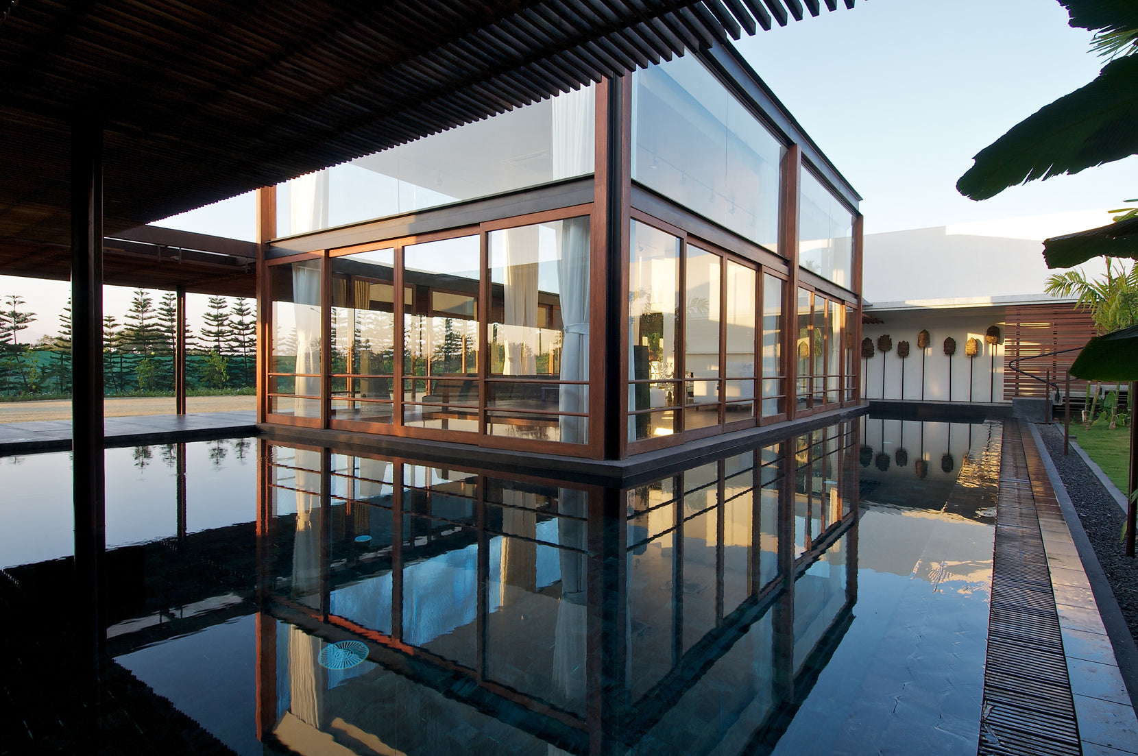 Glazed room mirrored in the pool at first light, timber pergola running overhead