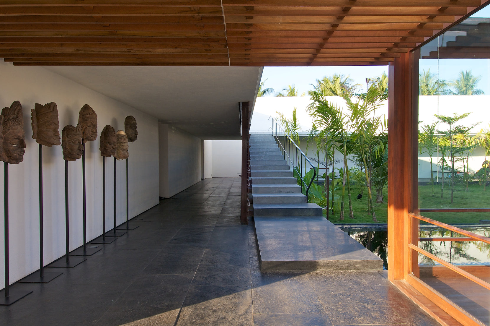Row of carved stone heads on stands lining the corridor, stair and courtyard beyond