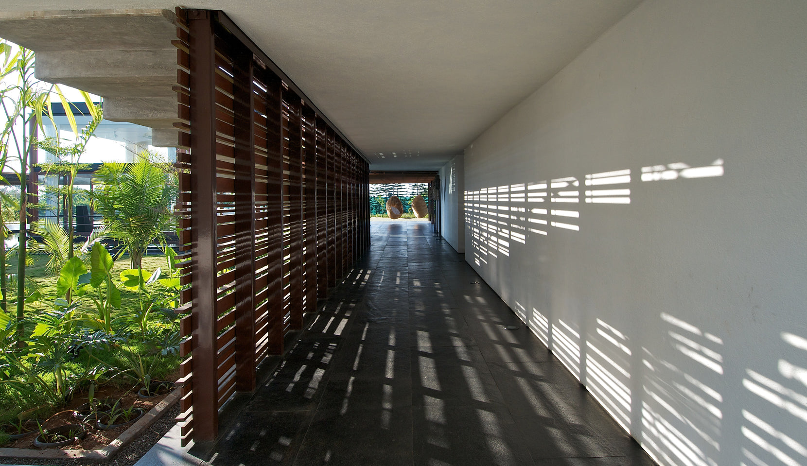 Slat screen casting bars of light across the white wall of the long stone-floored passage