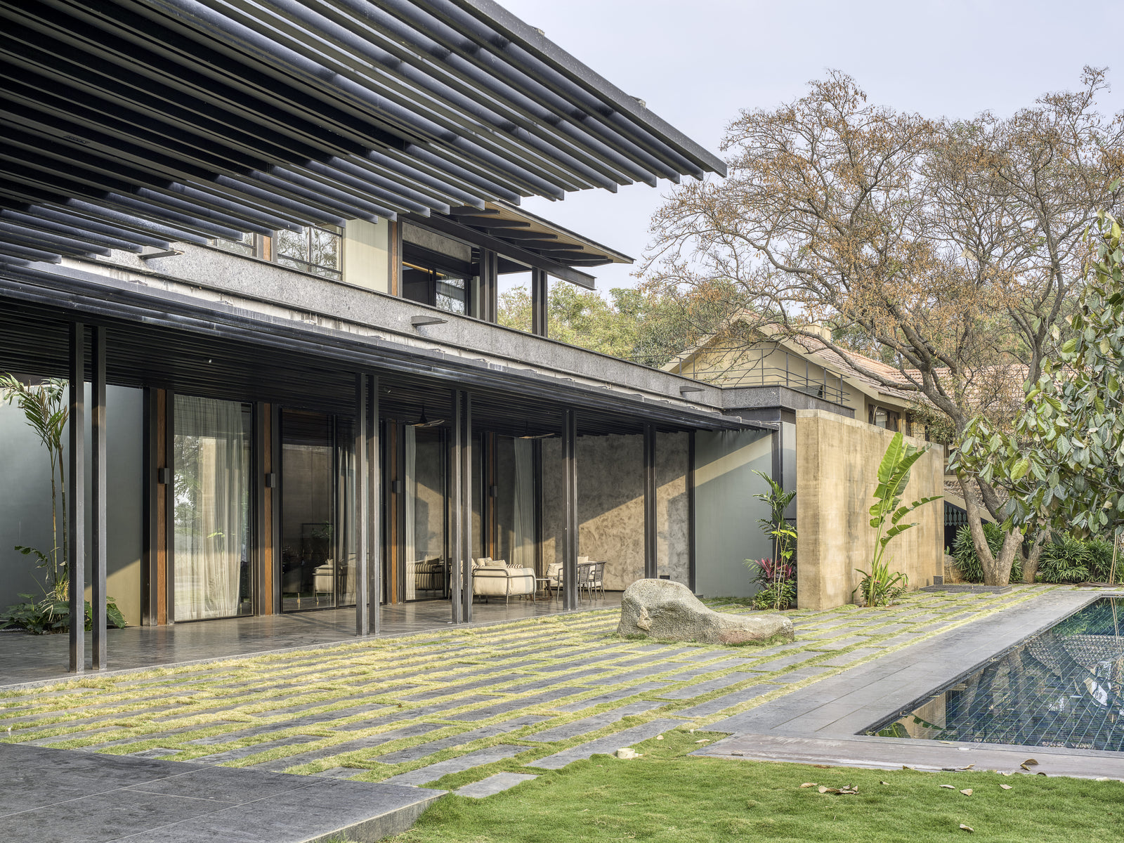 Louvred verandah roof over sliding glass doors, grass-jointed stone paving running to the pool