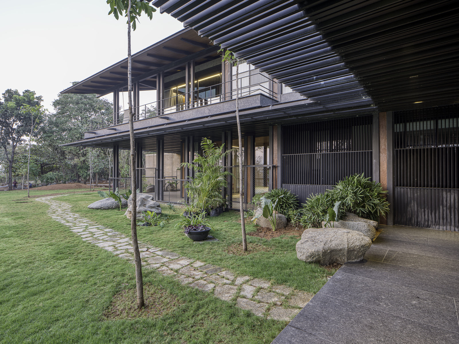 Stepping-stone path crossing the lawn towards the shaded lower verandah and its steel louvres