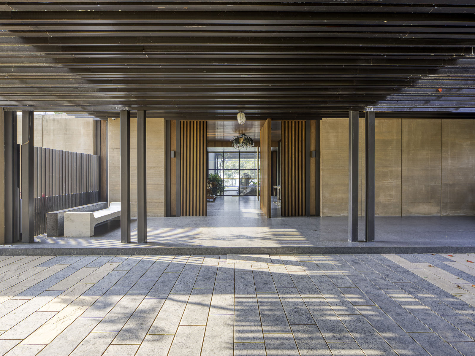 Entrance undercroft framed by slim steel columns and rammed earth walls, looking through to the garden