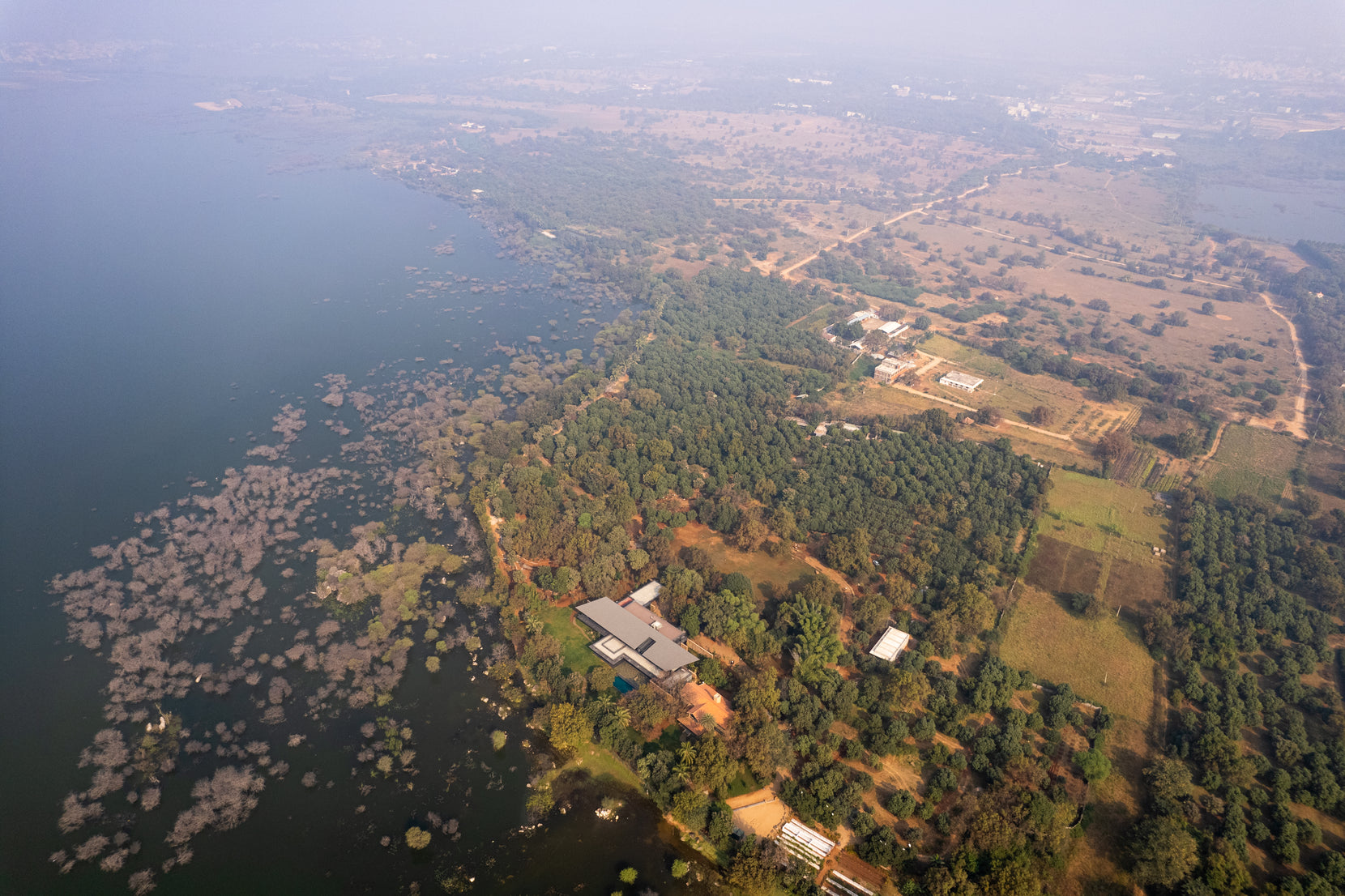 Aerial over the lake at Hyderabad showing Lakeshore House tucked into the wooded shoreline