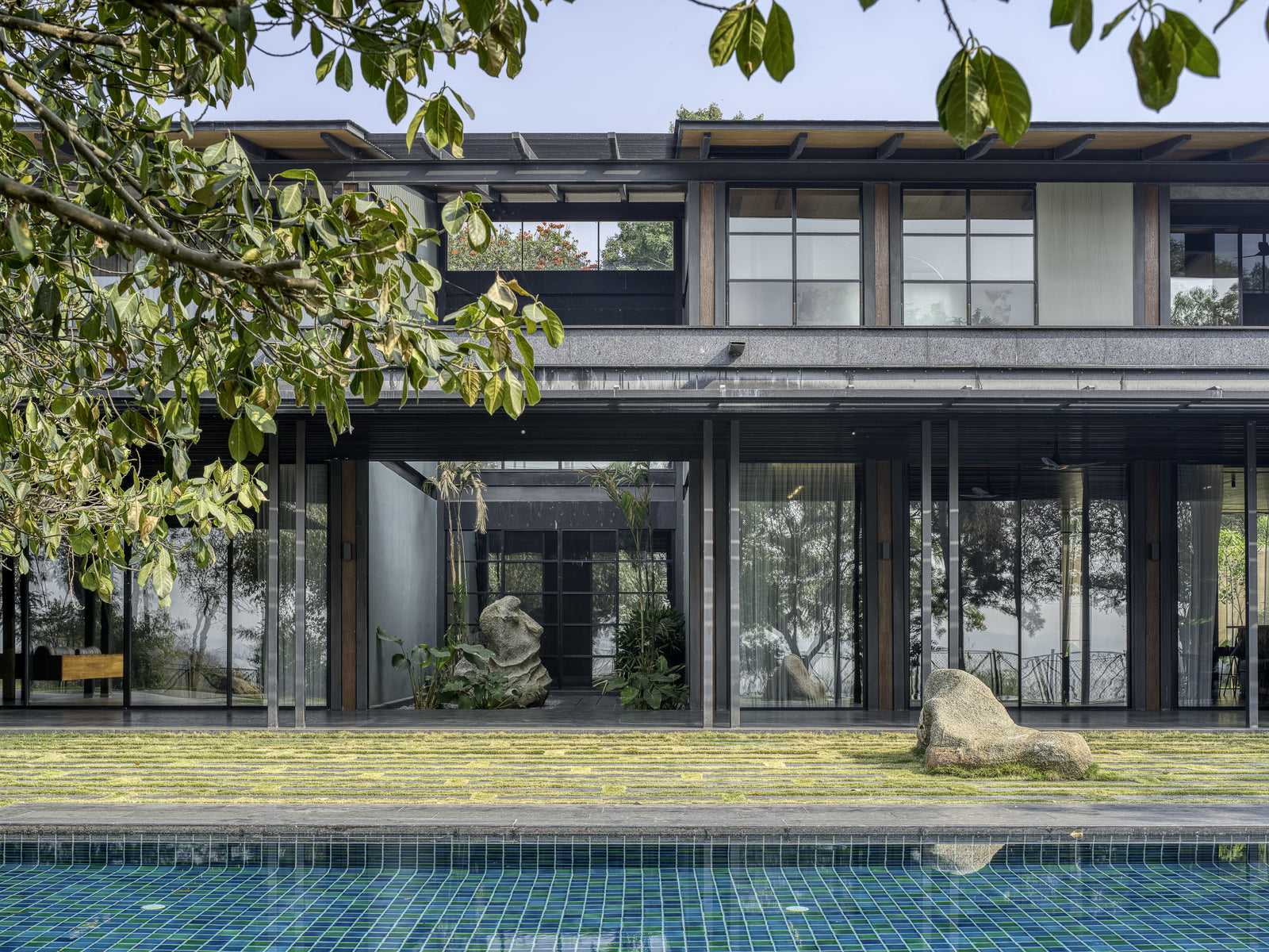 Glazed ground floor and inner court seen across the pool through overhanging foliage