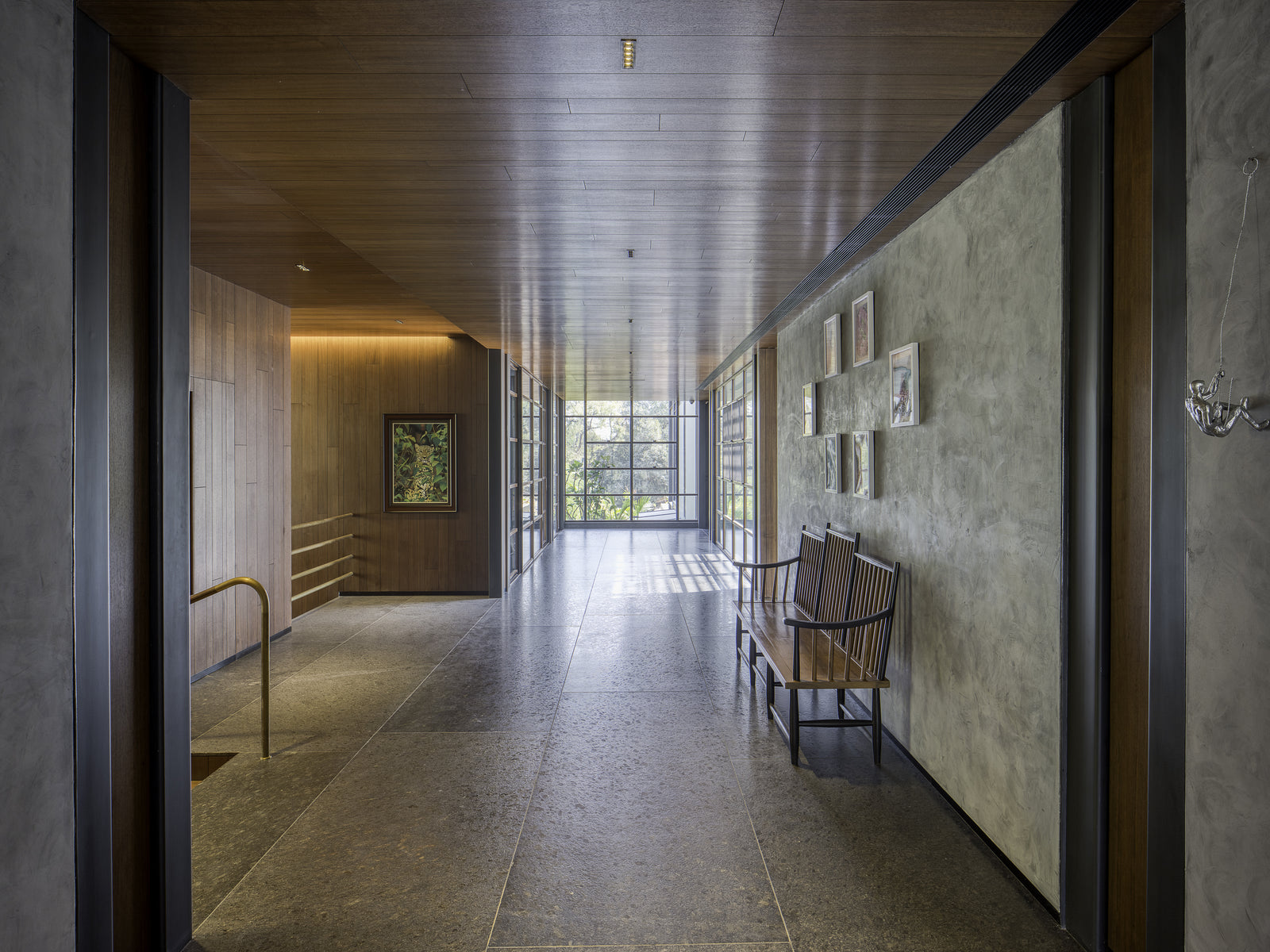 Corridor under a timber ceiling, stone floor and a caned bench below framed drawings