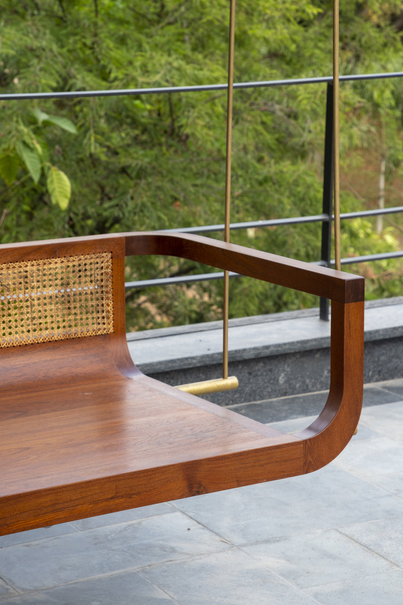 Detail of the teak and cane swing bed, its brass suspension rod against the terrace railing
