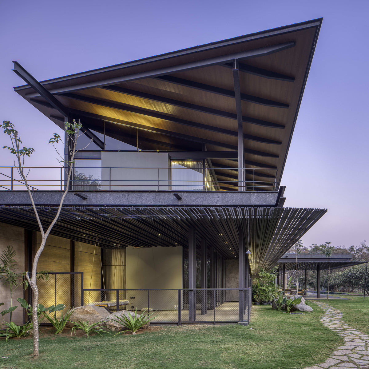 Lakeshore House at dusk, its cantilevered metal roof spreading over a lit upper terrace