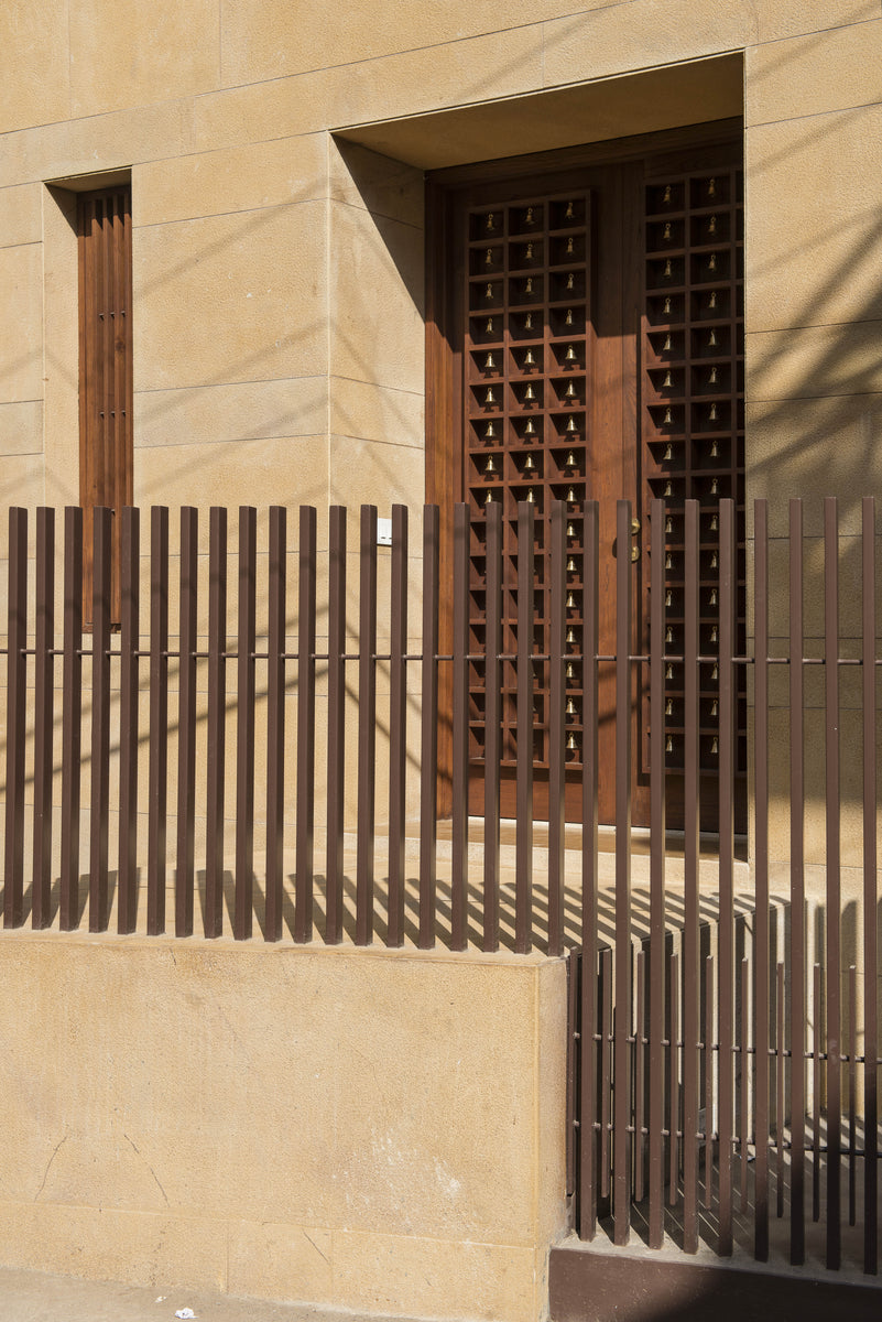 Sandstone entrance wall with a slatted gate and a teak door set with rows of brass bells
