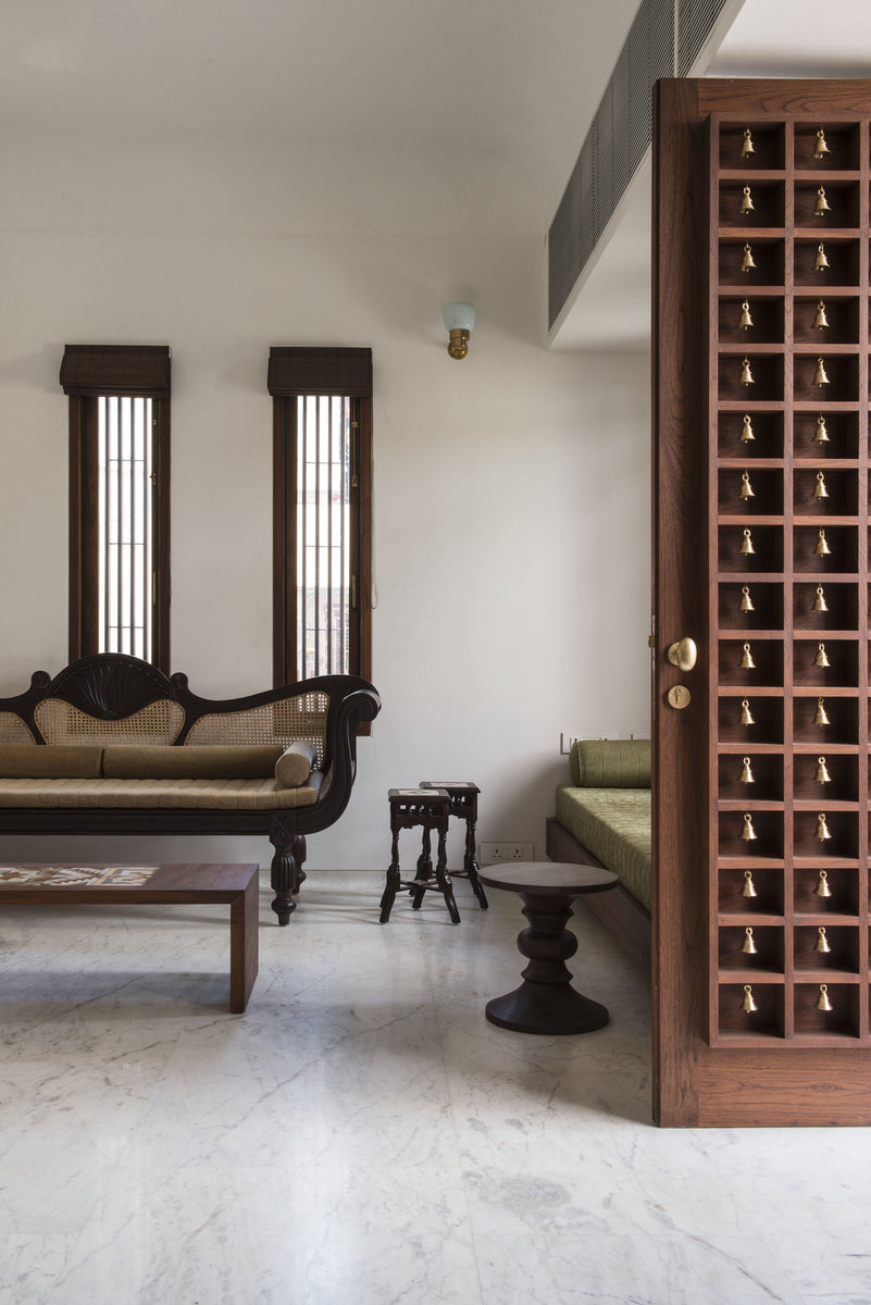 Living room in marble and white plaster, a carved settee beside the brass-bell teak screen