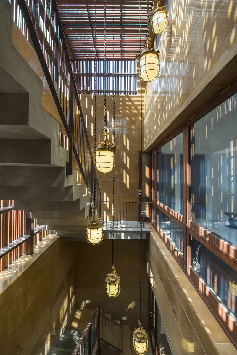 Light shaft with hanging glass lanterns, the concrete stair climbing to the timber grille roof