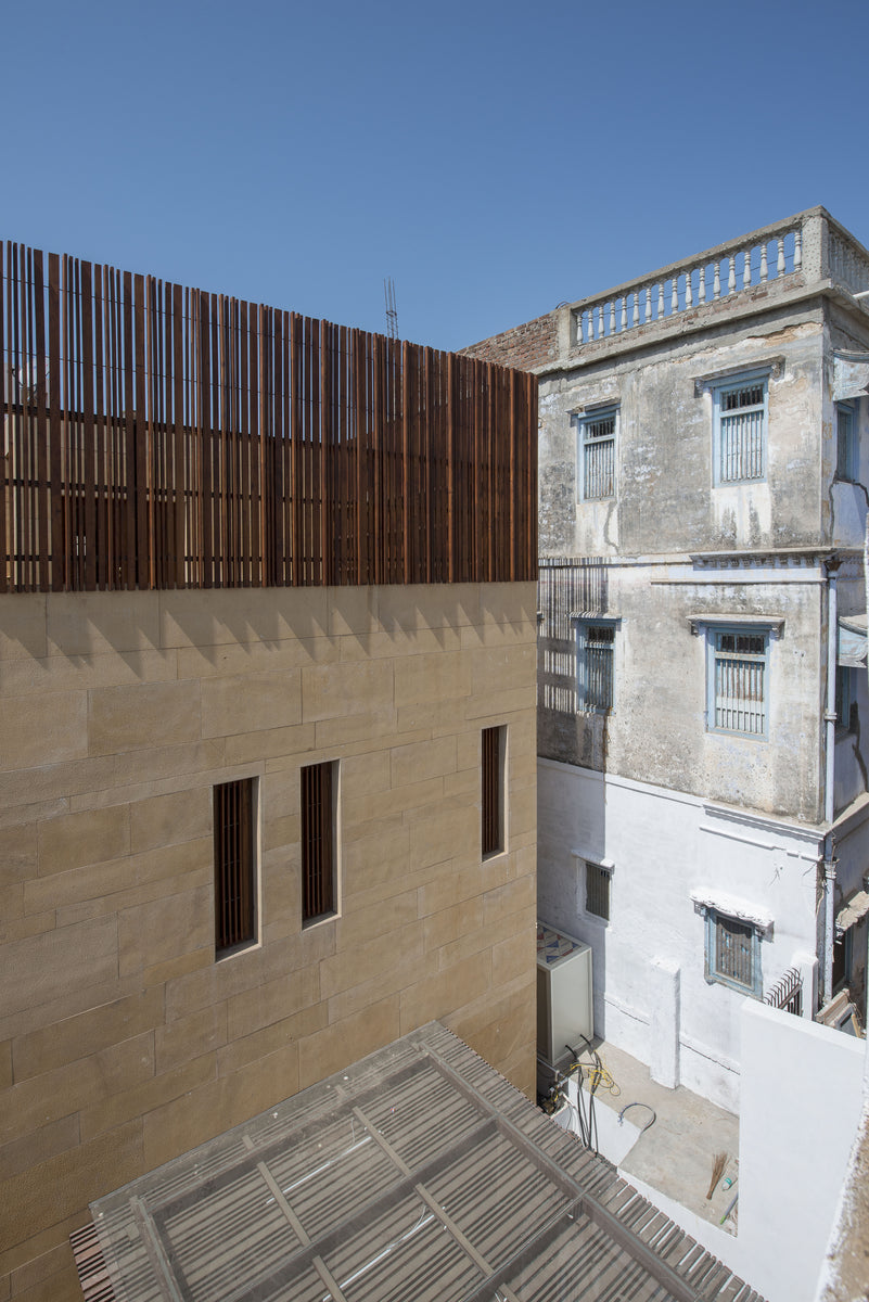 Sandstone wall with slit windows and timber screen above, an old neighbouring house alongside