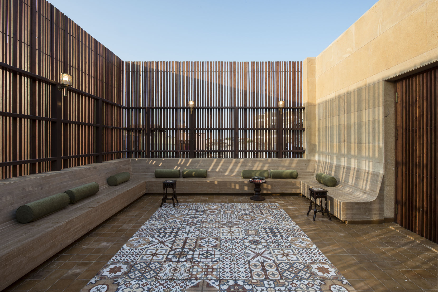 Roof terrace enclosed by timber screens, with built-in seating around a patterned tile carpet