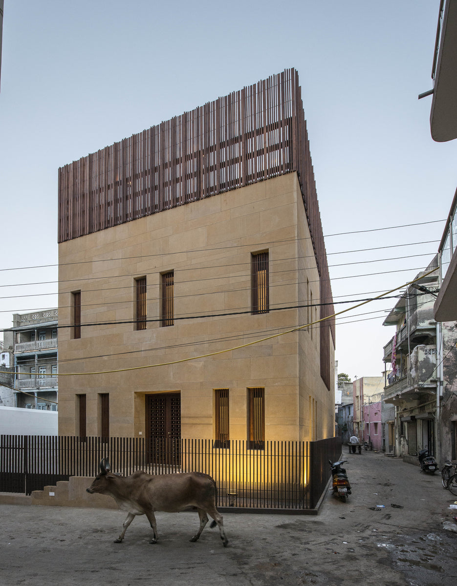 Mandvi House in Kutch, its sandstone street front capped by a timber screen, a cow passing at dusk