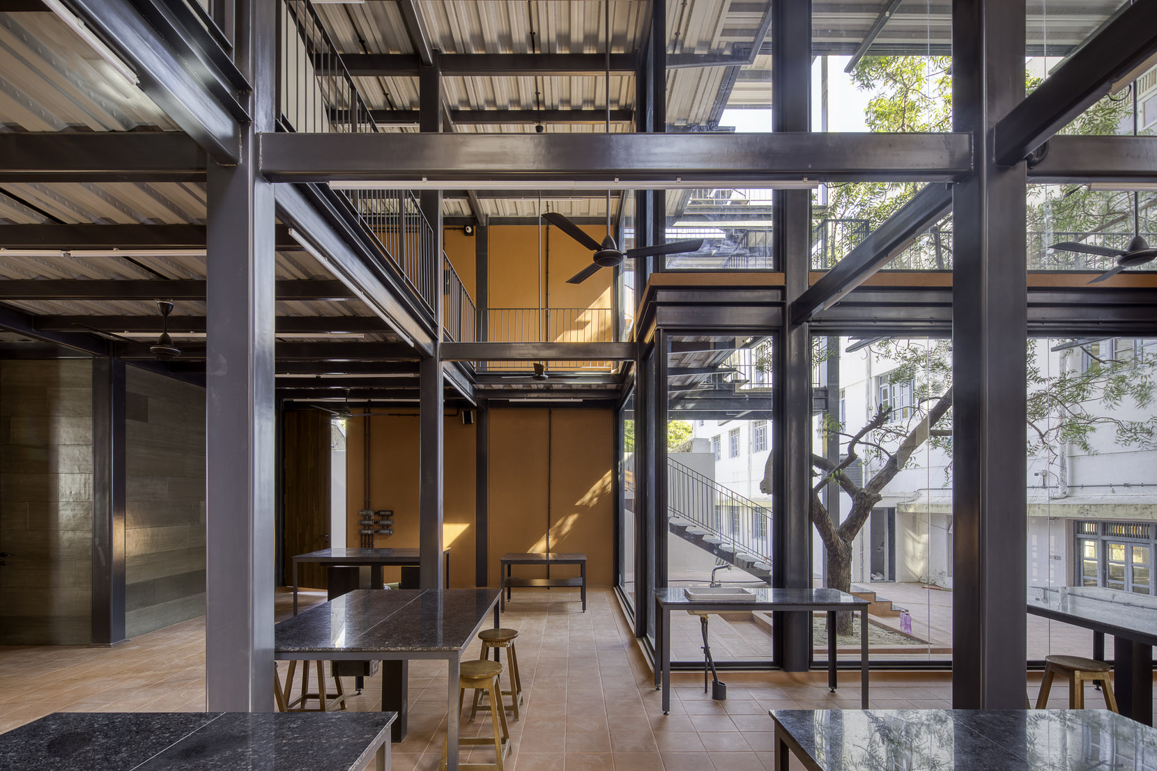 Double-height laboratory with exposed steel frame and stone-topped benches beside the courtyard tree