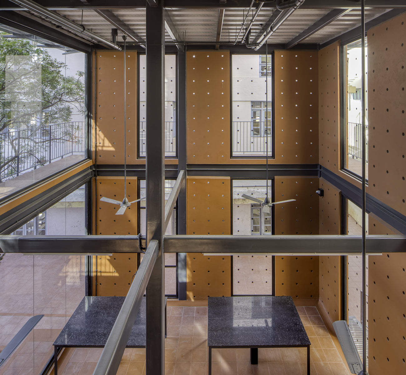 Atrium seen through glass, ochre panels and steel beams above tiled floors and stone-topped tables