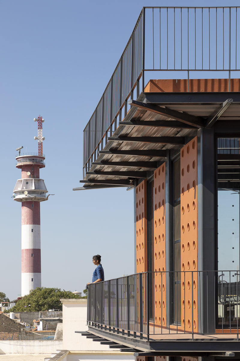 Rooftop terrace edge with the striped Mandvi lighthouse beyond and a student at the railing