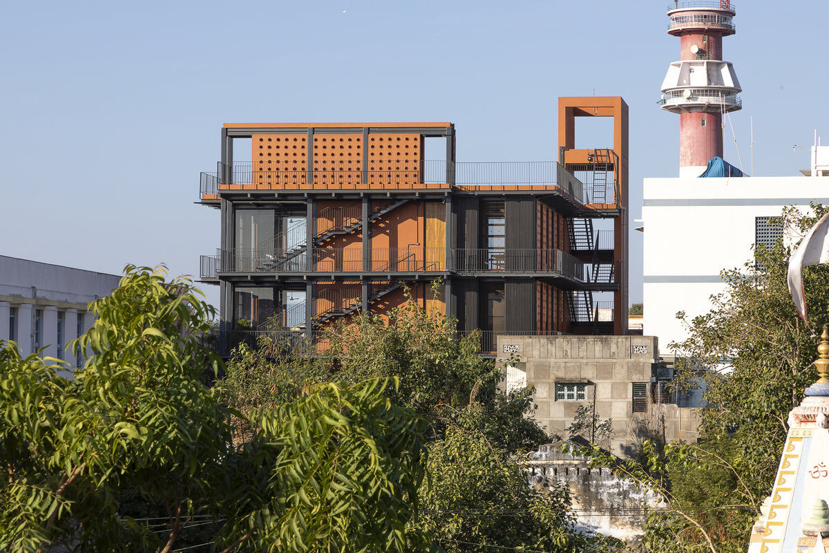 Mandvi Lab rising above the treetops in corten and steel, the town lighthouse alongside