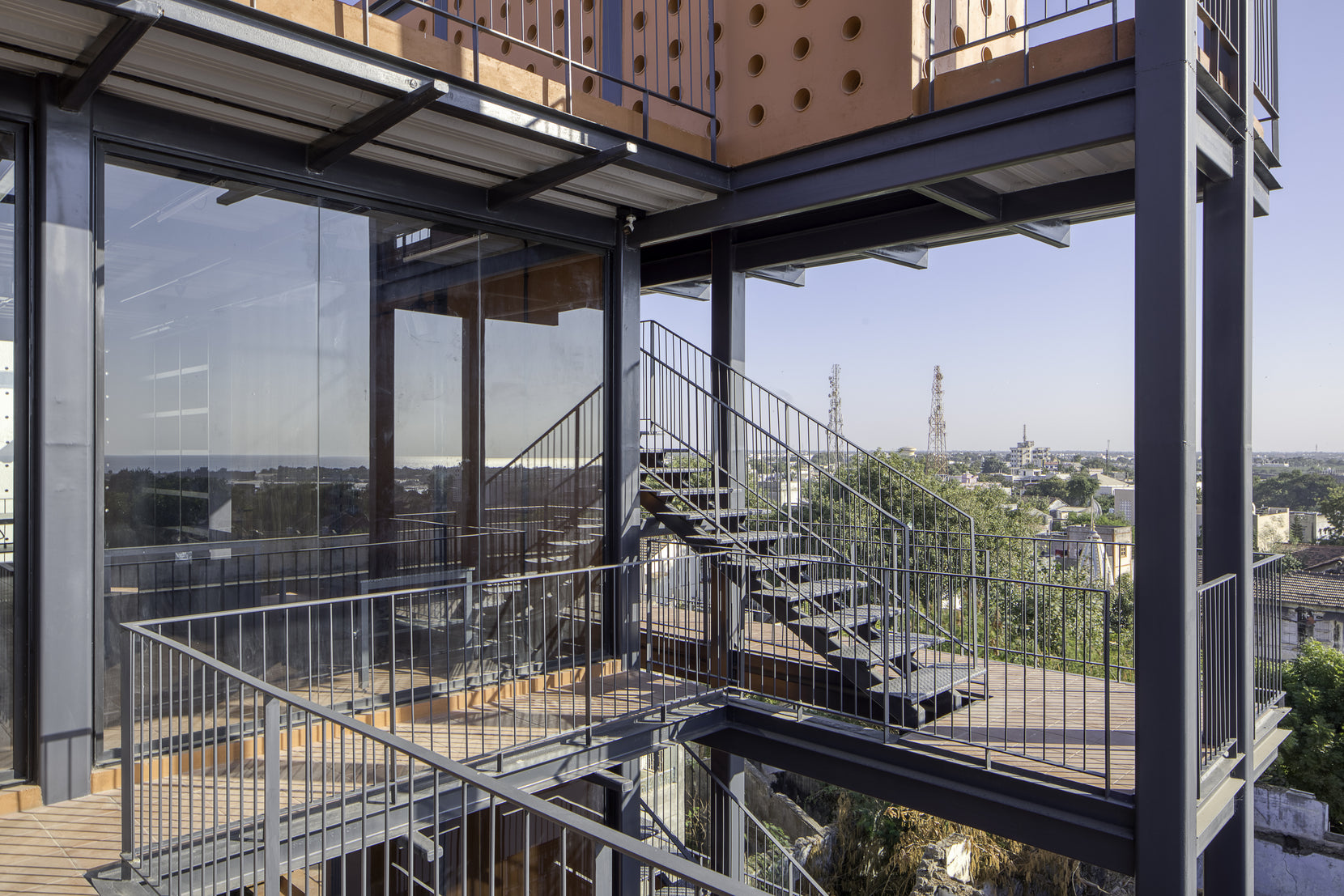 External steel stair and walkway wrapping the glazed floors, town rooftops in the distance