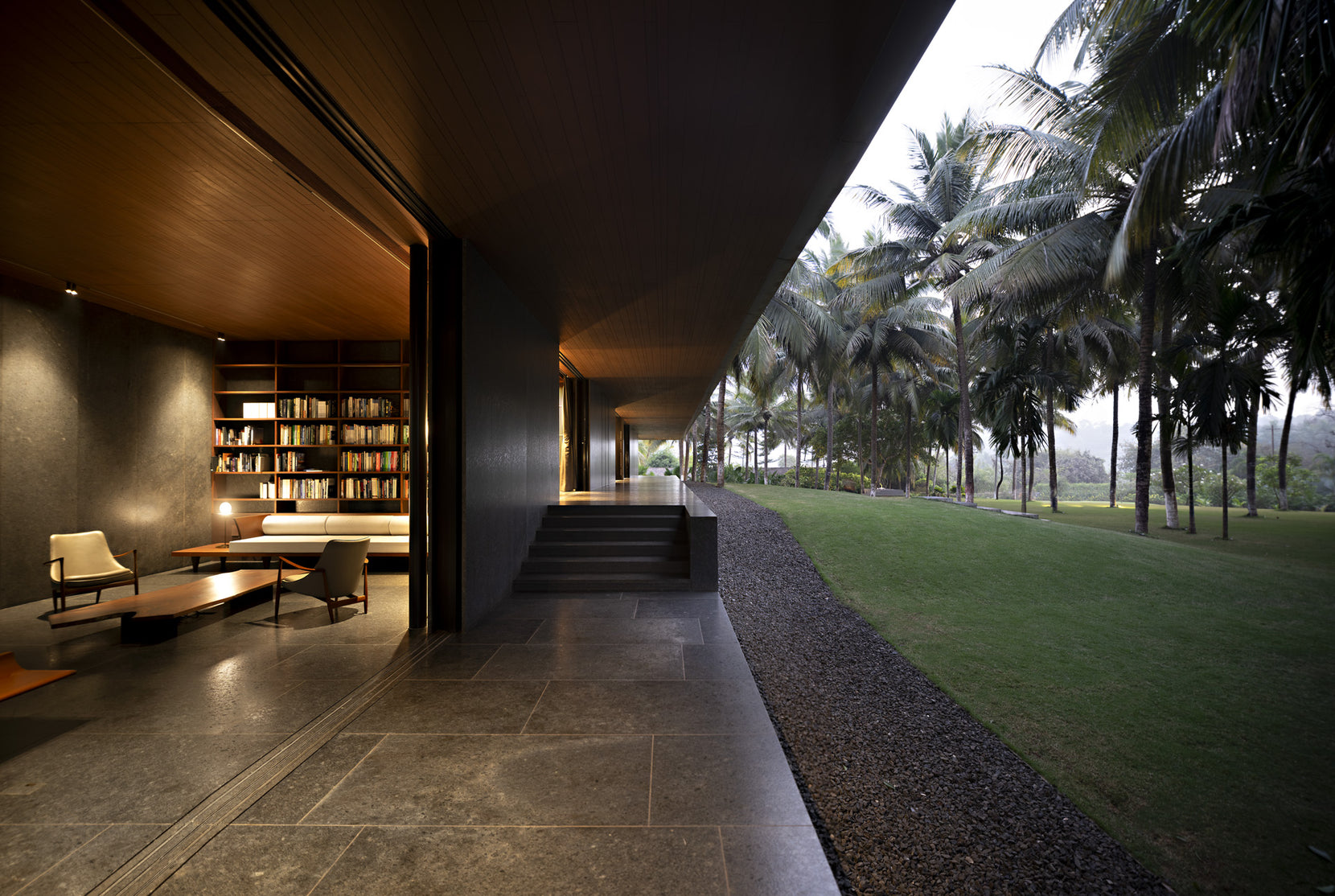 Circumambulatory verandah running past the library, gravel edge and palms to one side