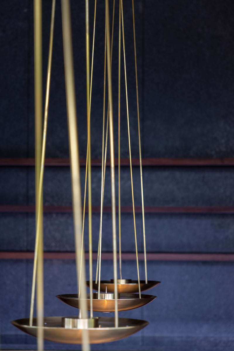 Brass dish pendant lights suspended on slender rods against a dark stone wall