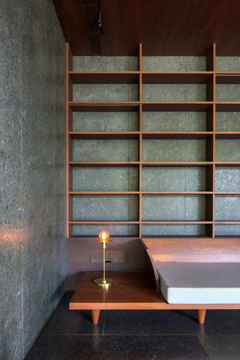 Teak shelving over green stone panels, with a low daybed and brass table lamp