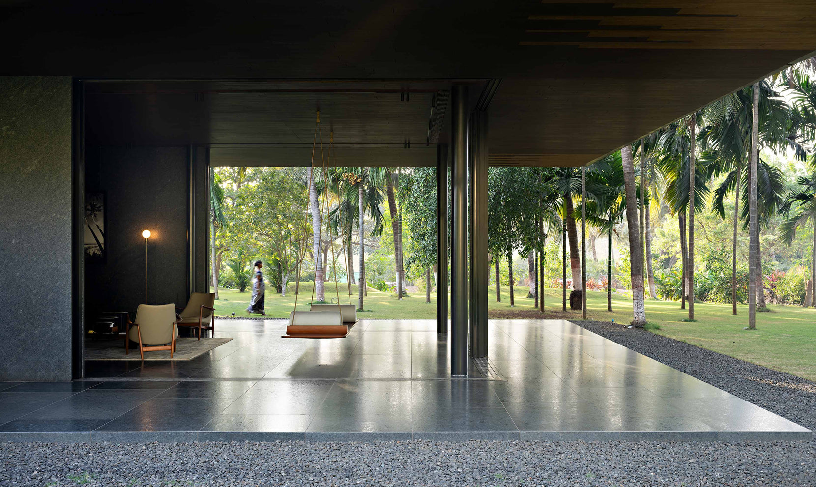 Swing seat hung in the open circulation spine, palms and lawn framed on both sides
