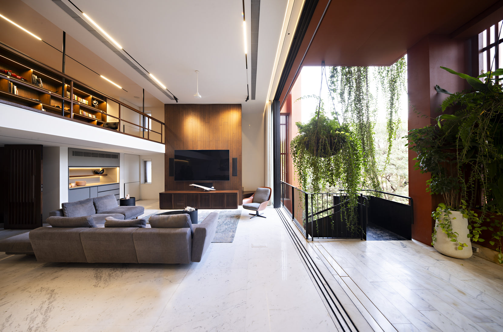 Living room with teak panelling and a wall-mounted screen beside sliding glazing to a fern-hung terrace