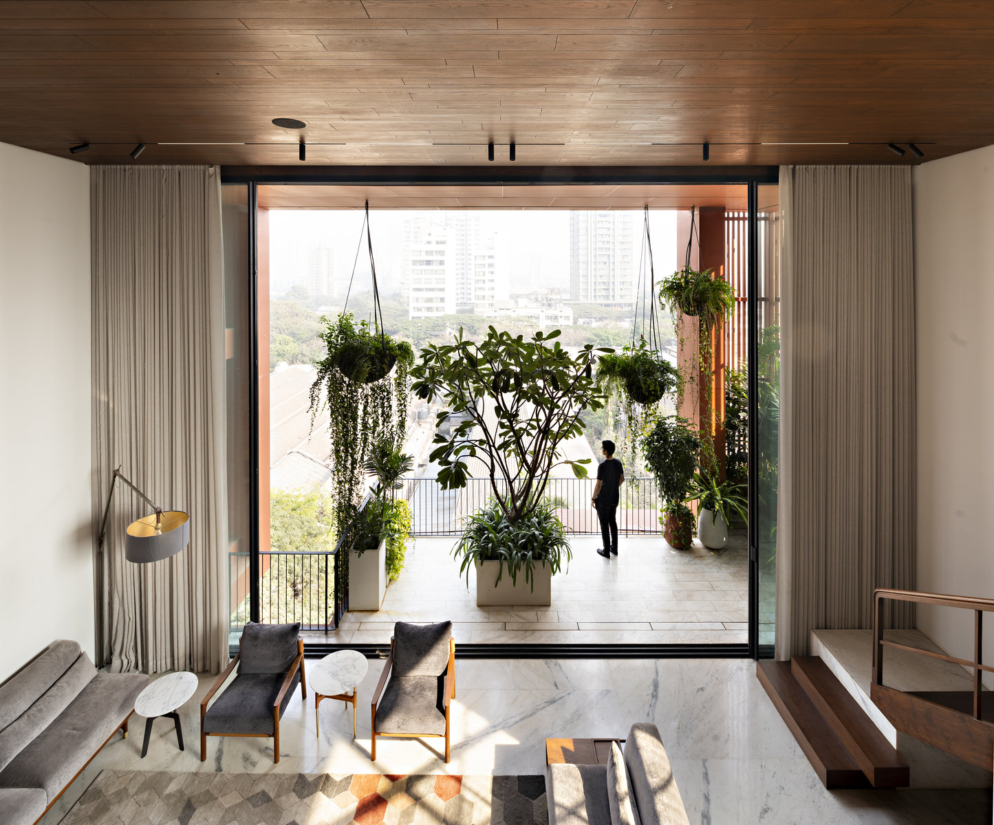 Sitting room framed by linen curtains, looking through to a planted verandah where a man stands