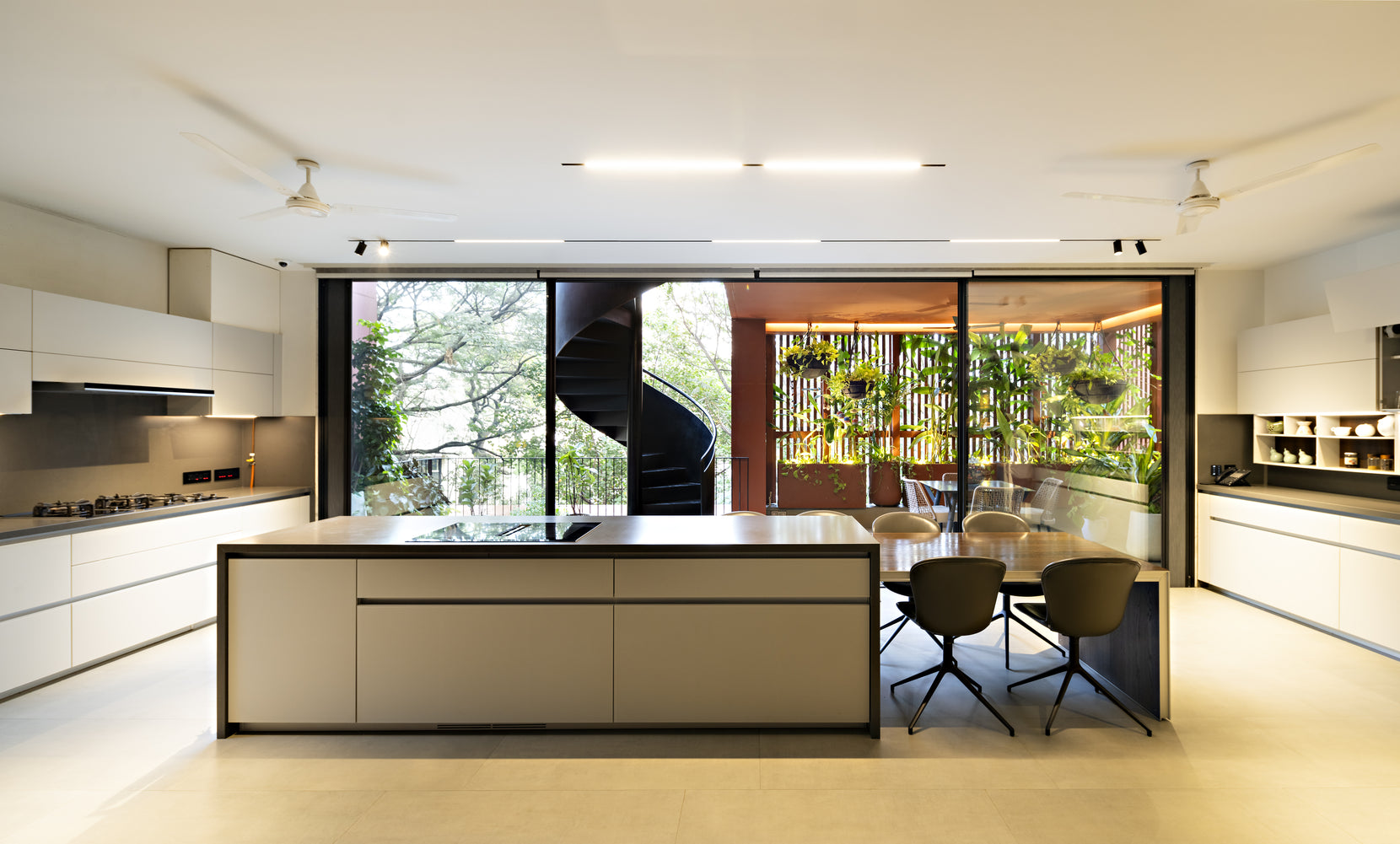 Kitchen island in pale joinery, the black spiral stair visible through full-height glazing