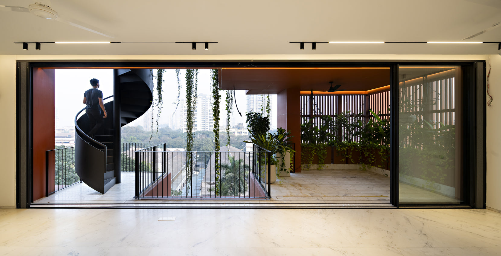 Sliding walls opened wide onto a terrace, a figure descending the black spiral stair