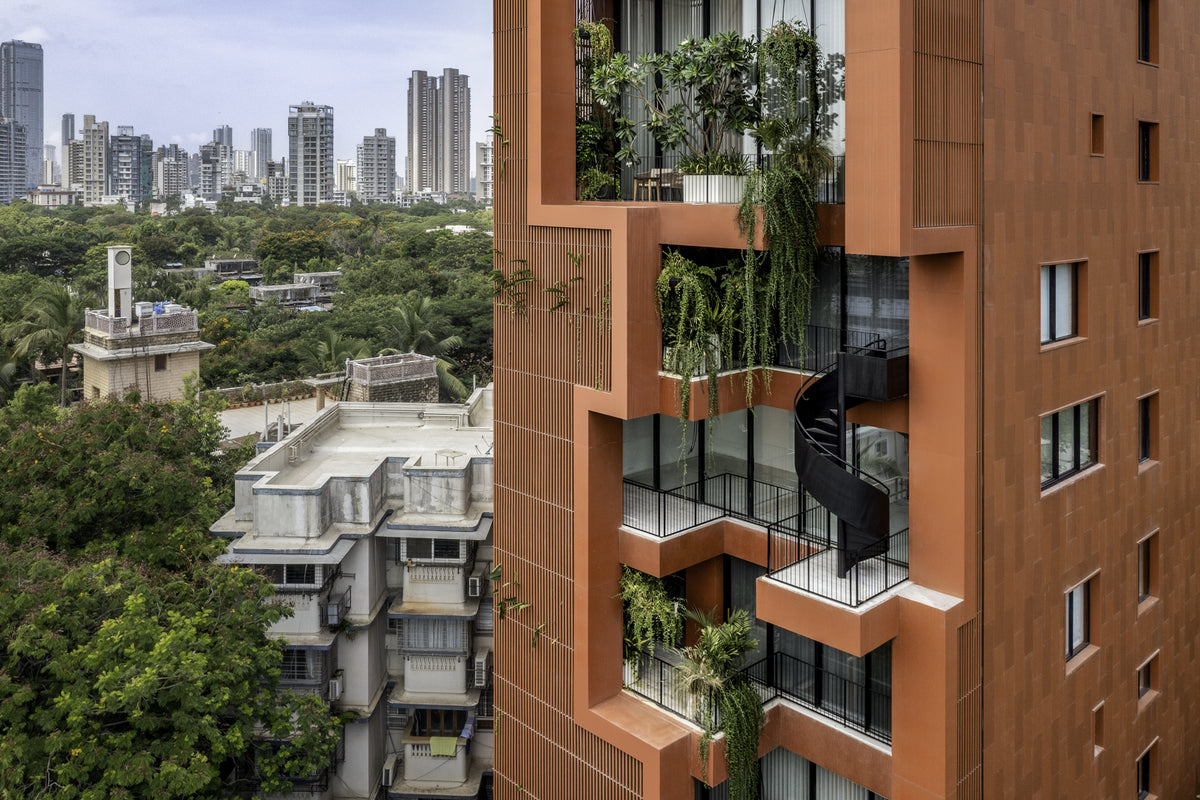 Sarvasva, a terracotta-clad tower in Mumbai, its planted balconies and black spiral stair above leafy roofs