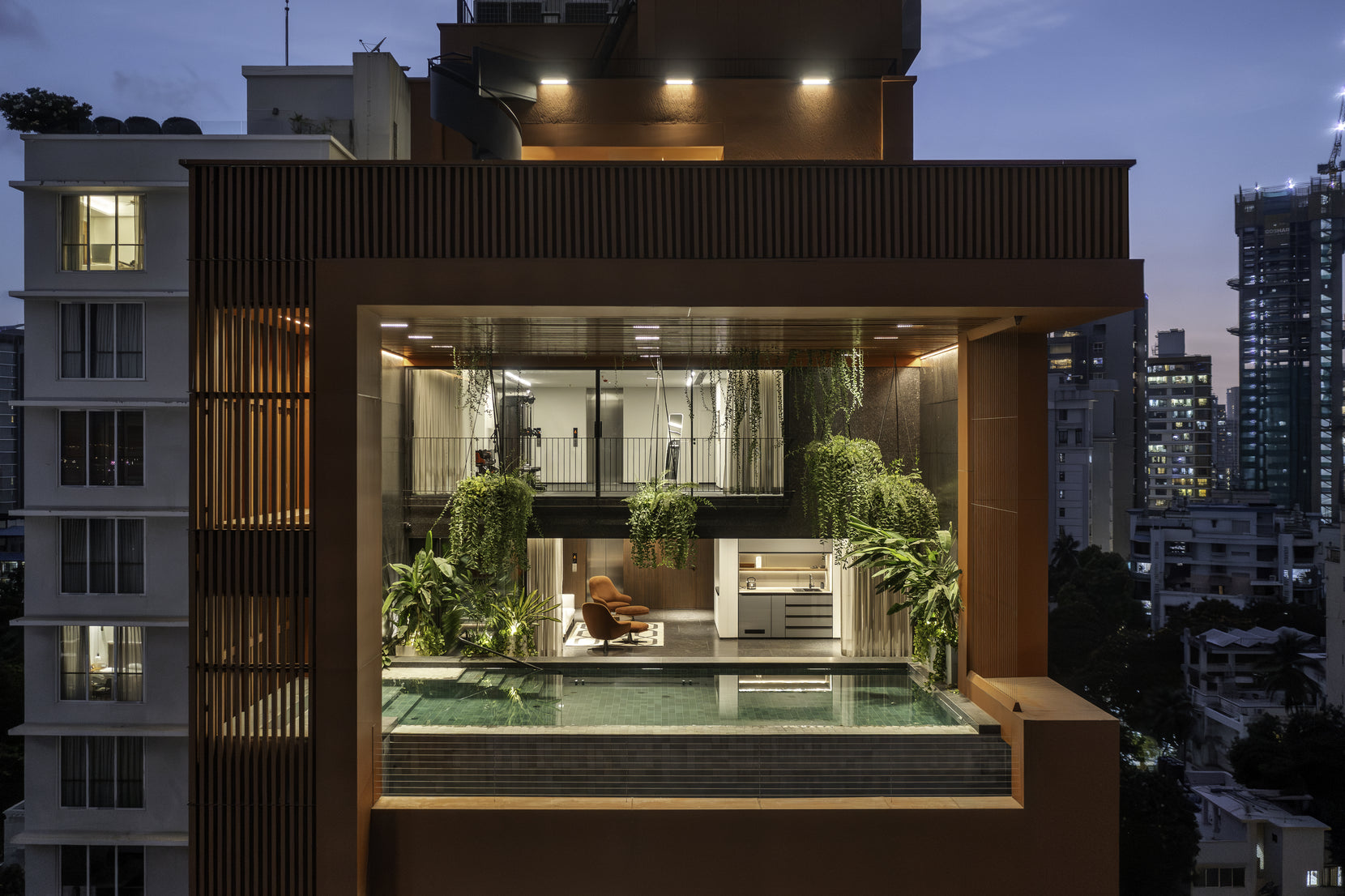 Double-height pool terrace glowing at nightfall, glazed and planted within its timber-lined frame